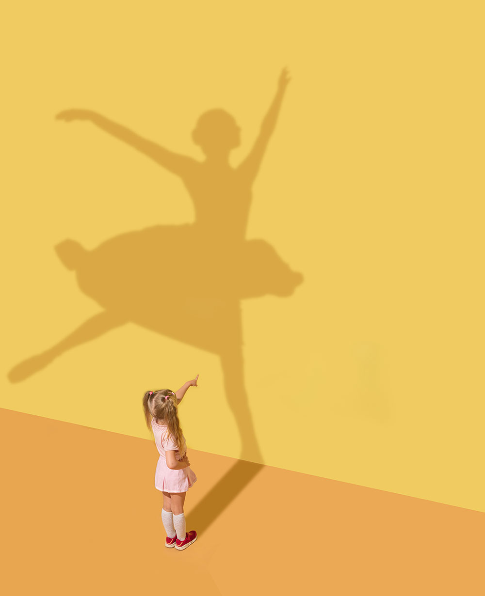 Bambina che guarda la sua ombra riflessa sul muro. L'ombra rappresenta una ballerina adulta